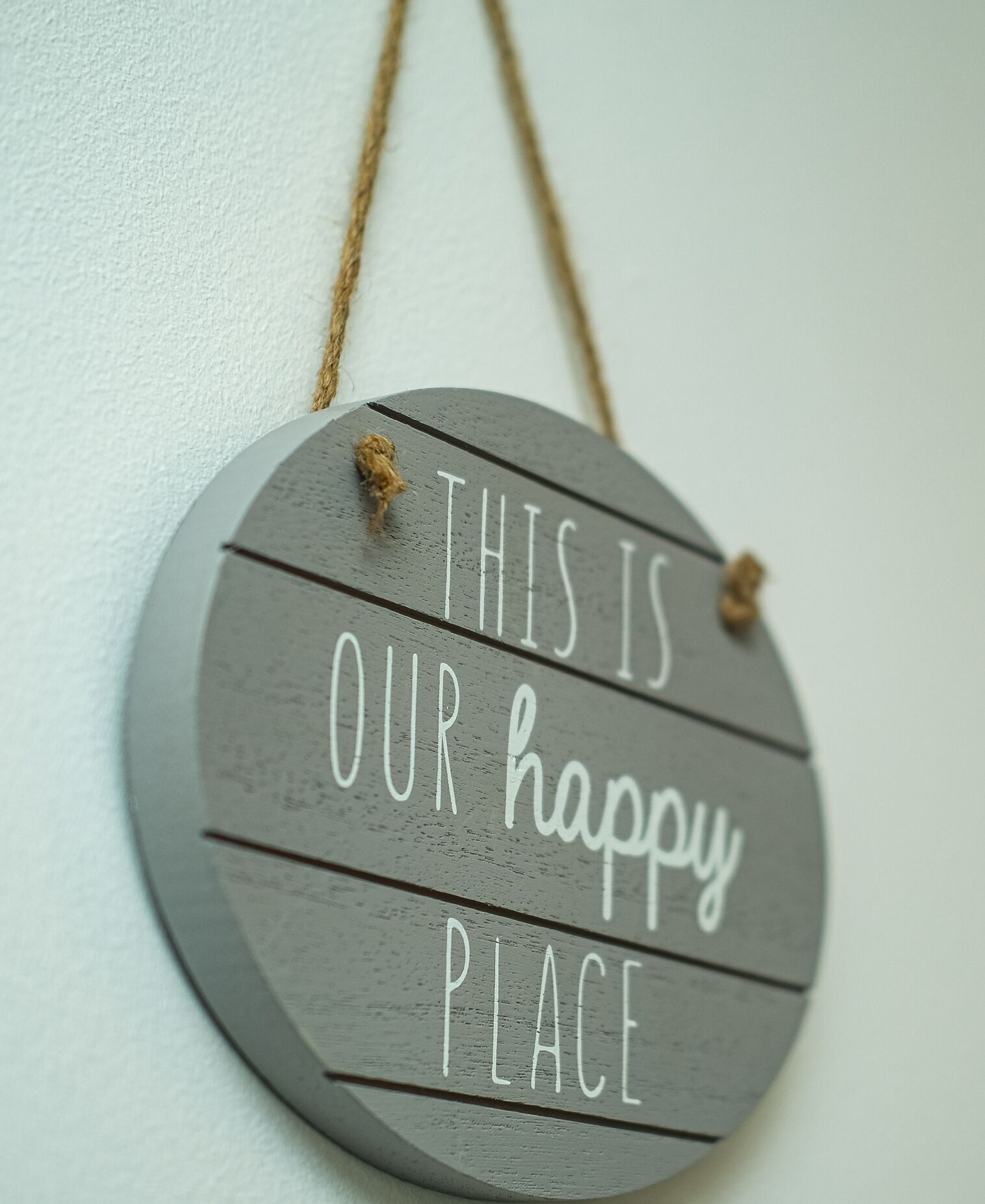A circular sign with the text "THIS IS OUR happy PLACE" hanging on a white wall.