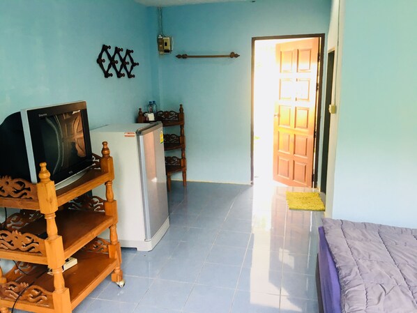 A room with a TV on a wooden stand, a refrigerator, a wooden chair, and a bed.