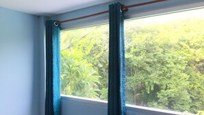 Una habitación con ventana, cortinas y vistas al exterior, con abundante vegetación.