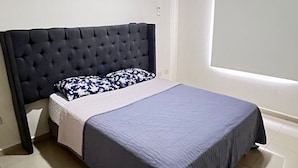 Ein Schlafzimmer mit einer gesteppten Kopfteil, einem Bett mit blauer Bettdecke, einem weißen Kissen und einem Fenster mit Jalousien.