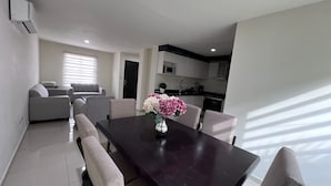 Ein modernes Wohnzimmer mit einem dunklen Holzesstisch, beigen Sofas und einer Vase mit Blumen.