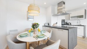 A modern kitchen with a central island, a dining area with a round table, and a pendant light.