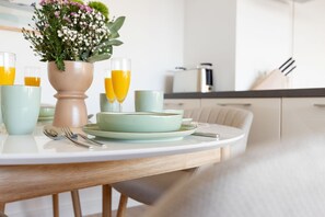 A dining table with a vase of flowers, two glasses of orange juice, and a plate with a bowl. - Lykke - Hochwertige Modern-skandinavische Ferienwohnung mit Balkon (Hörnum (Sylt))