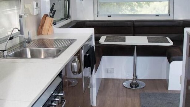 A compact kitchen with a sink, stove, and a dining area with a table and bench. - Longford Riverside Caravan Park (Longford)