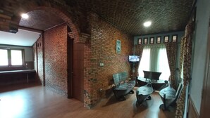 A room with a brick wall, wooden floor, a television mounted on the wall, and a window with curtains. - Kampung Turis Resort & Waterpark (Tegalwaru)