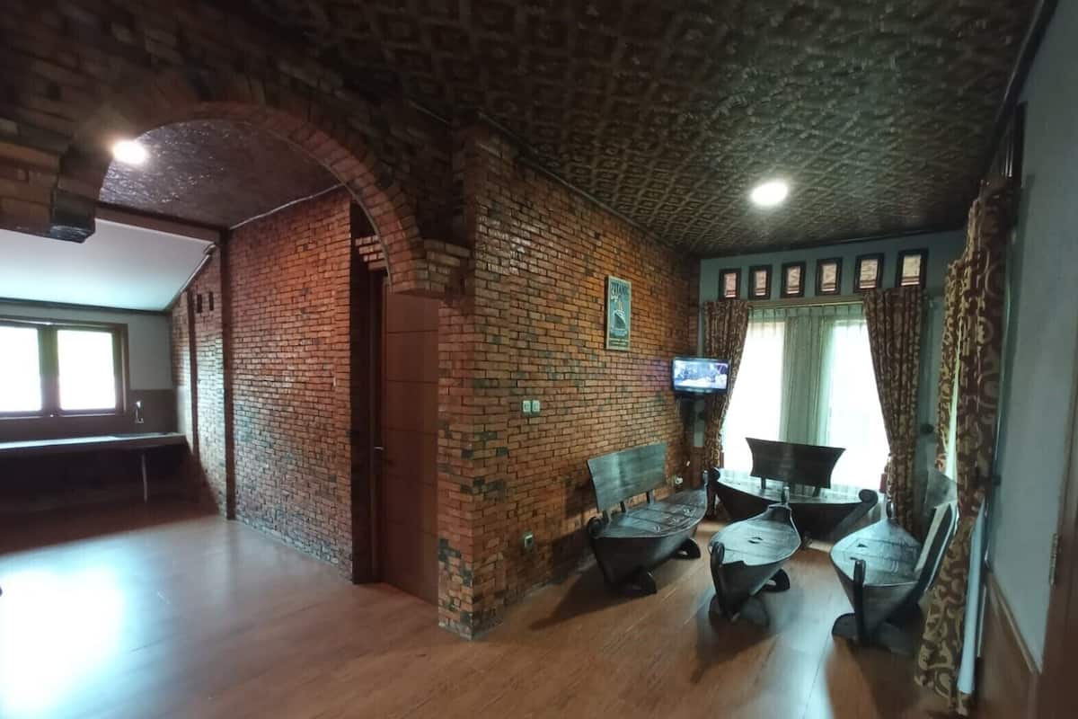 A room with a brick wall, wooden floor, a television mounted on the wall, and a window with curtains.