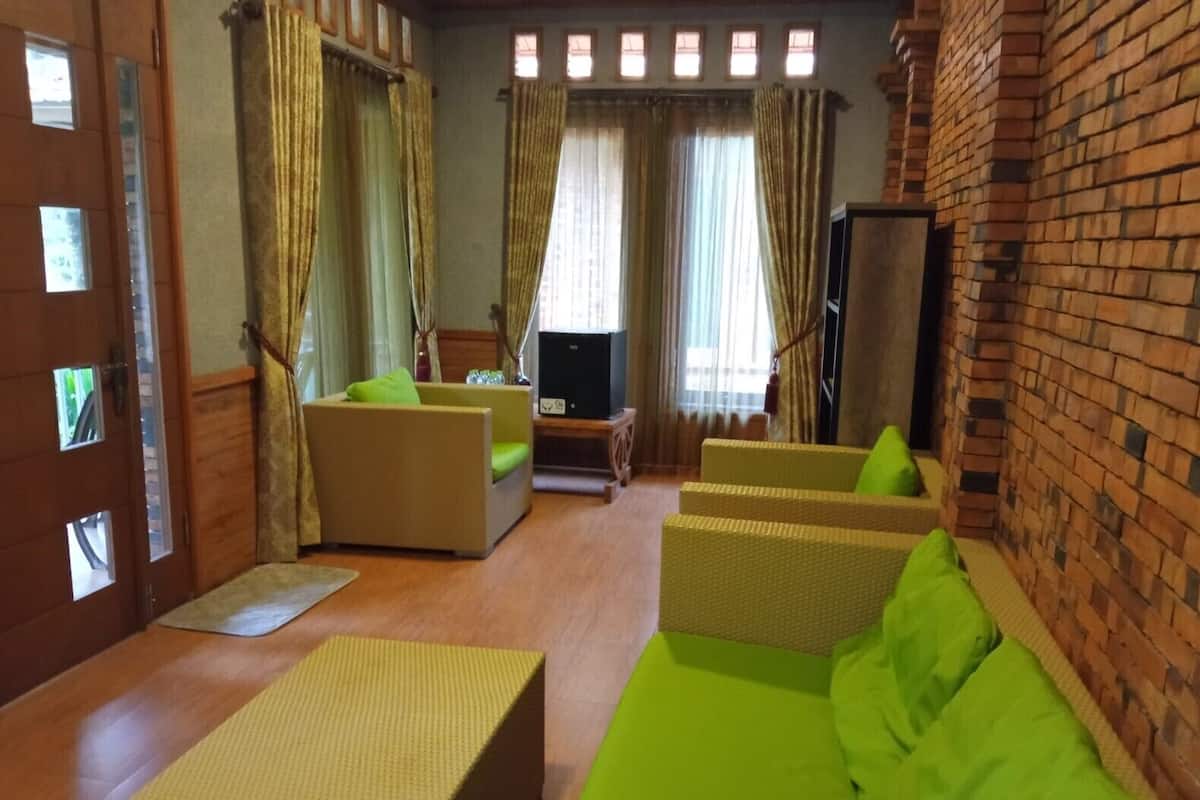 A cozy living room with a brick wall, a wooden door, and a television. There are two green sofas and a wooden coffee table.