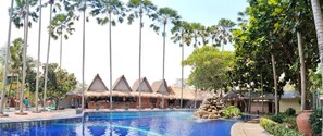A pool area with thatched-roof structures, palm trees, and a clear blue pool. - Kampung Turis Resort & Waterpark (Tegalwaru)