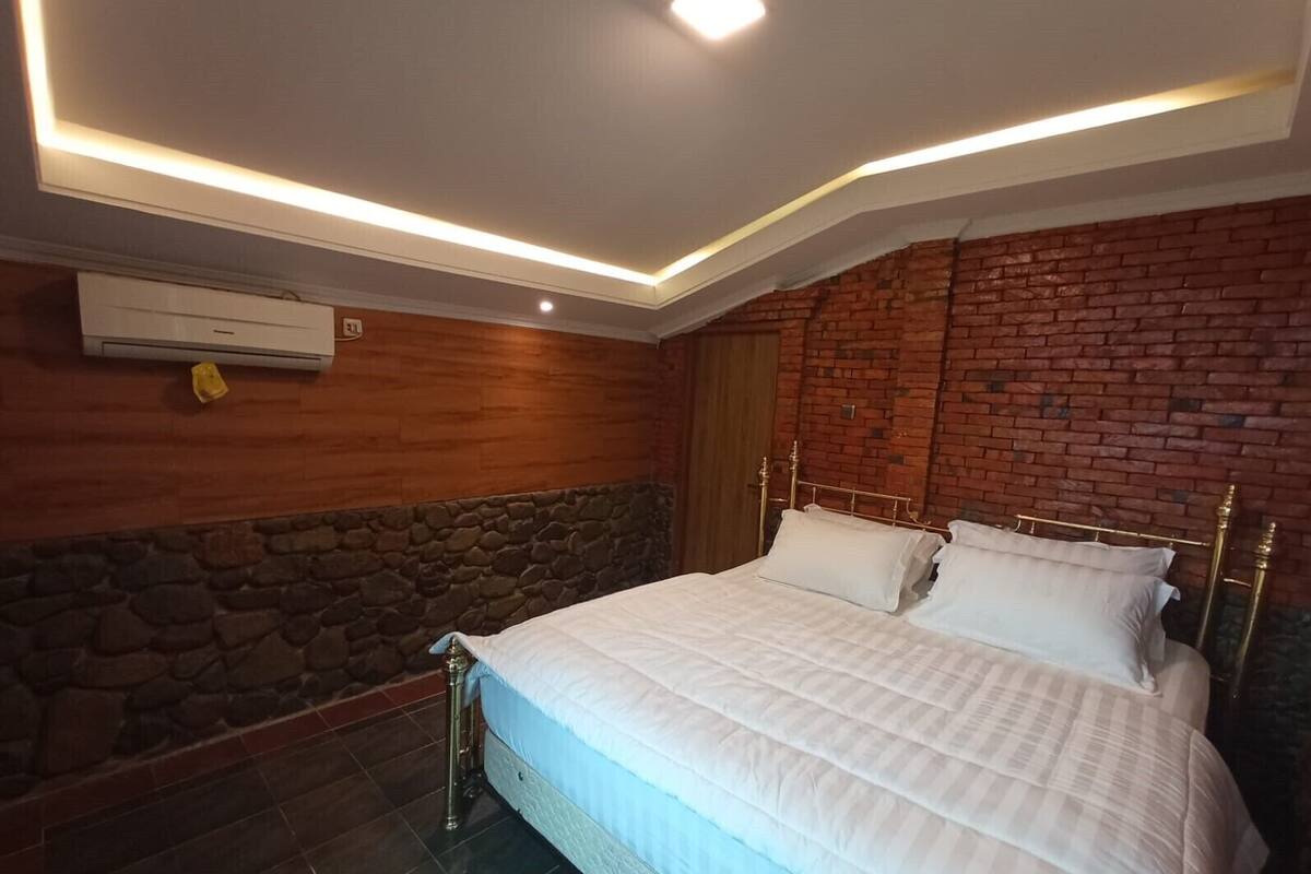 A bedroom with a brick wall, a stone accent wall, a bed with white bedding, and a modern ceiling light fixture.