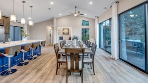 A spacious dining area with a high ceiling, pendant lighting, and a view of the outdoors through large windows.