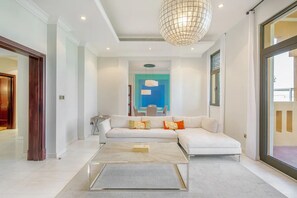 A modern living room with a white sofa, a glass coffee table, and a large chandelier.