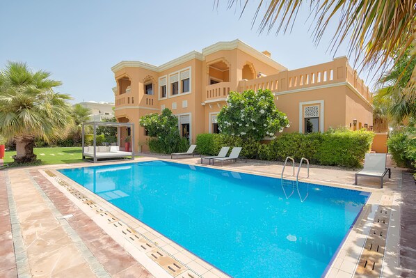 A swimming pool with a clear blue water, surrounded by a tiled deck.
