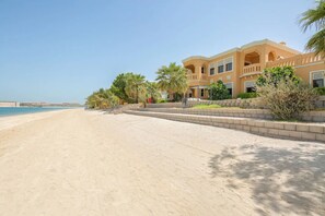 A beachfront property with a large building, palm trees, and a sandy beach.