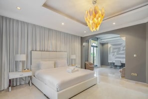 A modern bedroom with a large bed, a chandelier, and a view of a dining area.