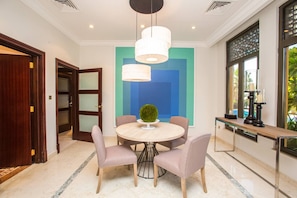 A dining area with a round table, four chairs, a central decorative plant, and pendant lighting.
