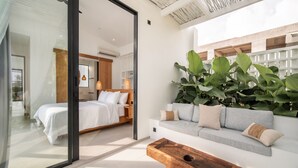 A modern hotel room with a glass partition, a bed, a sofa, and a wooden coffee table.