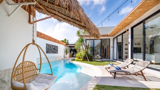 A modern outdoor pool area with a hanging chair, lounge chairs, and a thatched roof structure.
