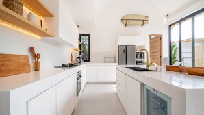 A modern kitchen with white cabinetry, a built-in oven, and a dishwasher. There are wooden shelves above the counter and a window providing natural light.