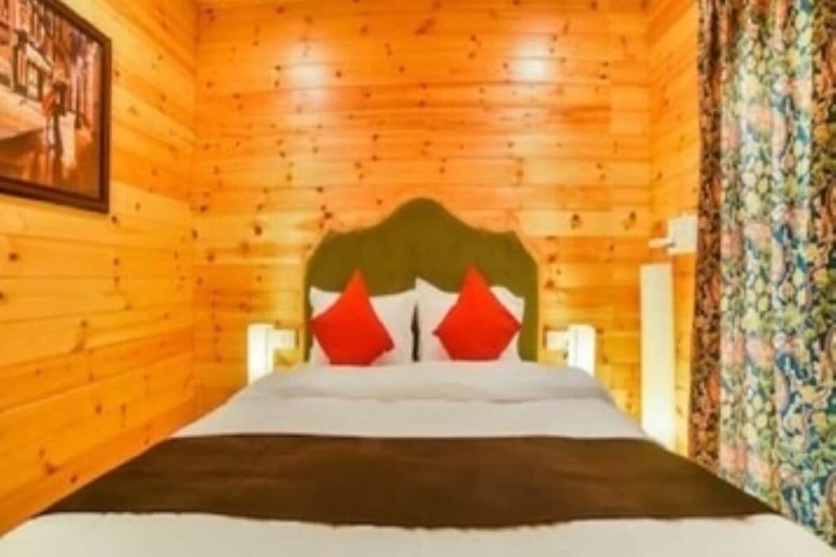A wooden cabin room with a bed, a headboard, and a painting on the wall.
