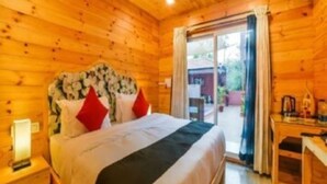 A wooden cabin room with a bed, a nightstand, a desk, and a sliding glass door leading to an outdoor area. - The Emerald Morjim (Morjim)