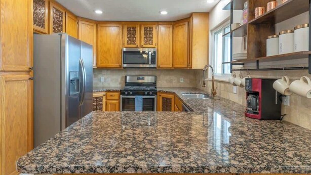 A kitchen with wooden cabinets, granite countertops, stainless steel appliances, and a coffee machine. - Spacious Family Home • Game Room • Pets Welcome (Orem)