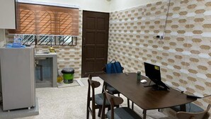 A small, compact kitchen with a refrigerator, sink, and a window with a view. There is a dining table with chairs and a fan on the wall. - Bukit Tinggi Homestay (Klang)