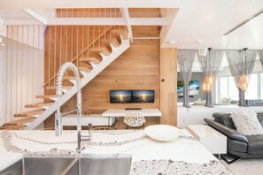 A modern living room with a wooden staircase, a flat-screen TV, and a sofa.