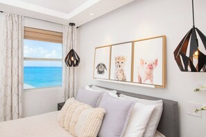 A bedroom with a bed, a window with curtains, and a wall with framed pictures.
