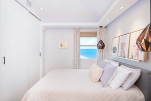 Um quarto com cama, janela com cortinas e vista para o mar.