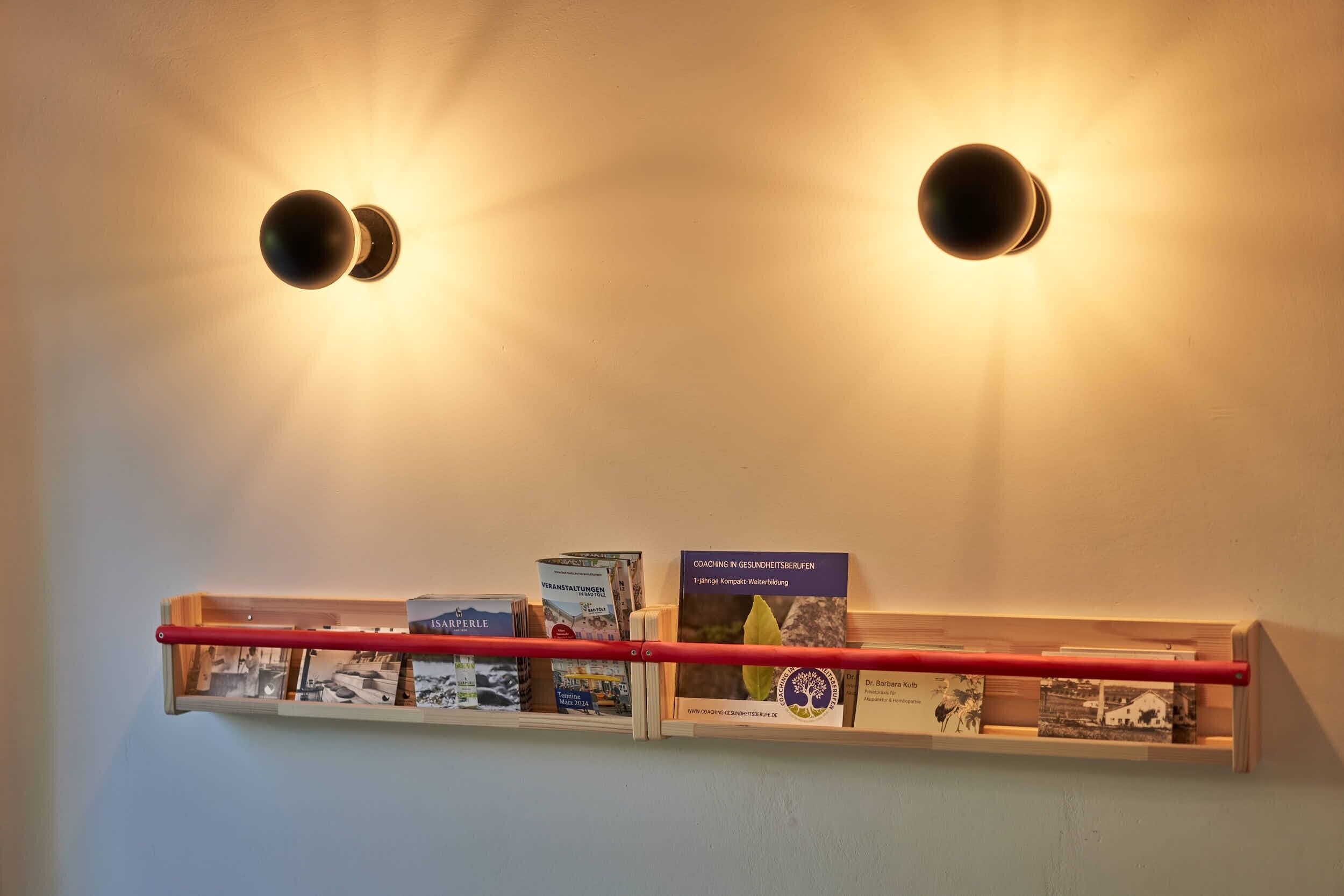 Una mensola a parete con libri e un'asta orizzontale rossa, illuminata da luci a soffitto.