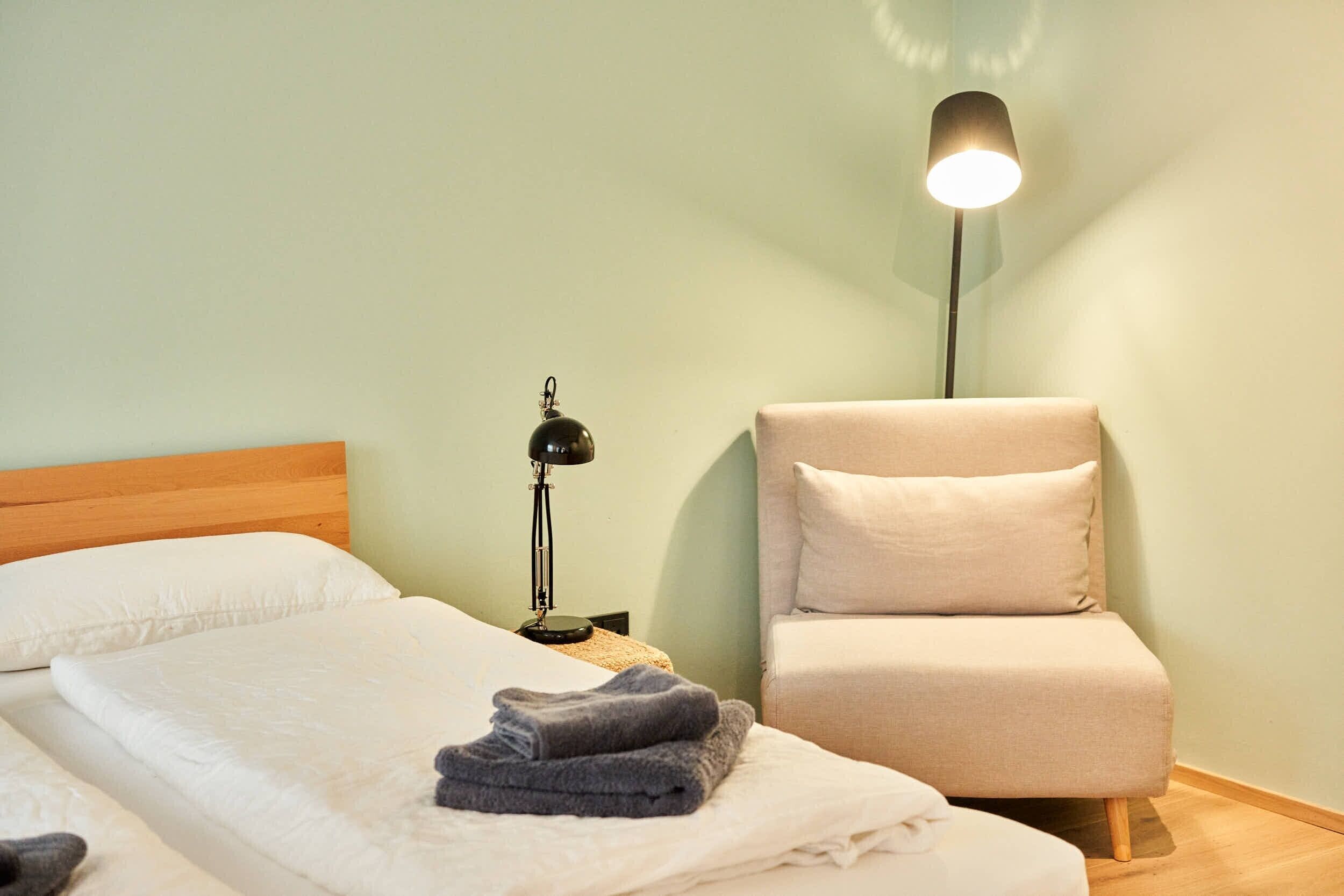 Une chambre d’hôtel avec un lit, une chaise, une lampe et un luminaire fixé au mur.