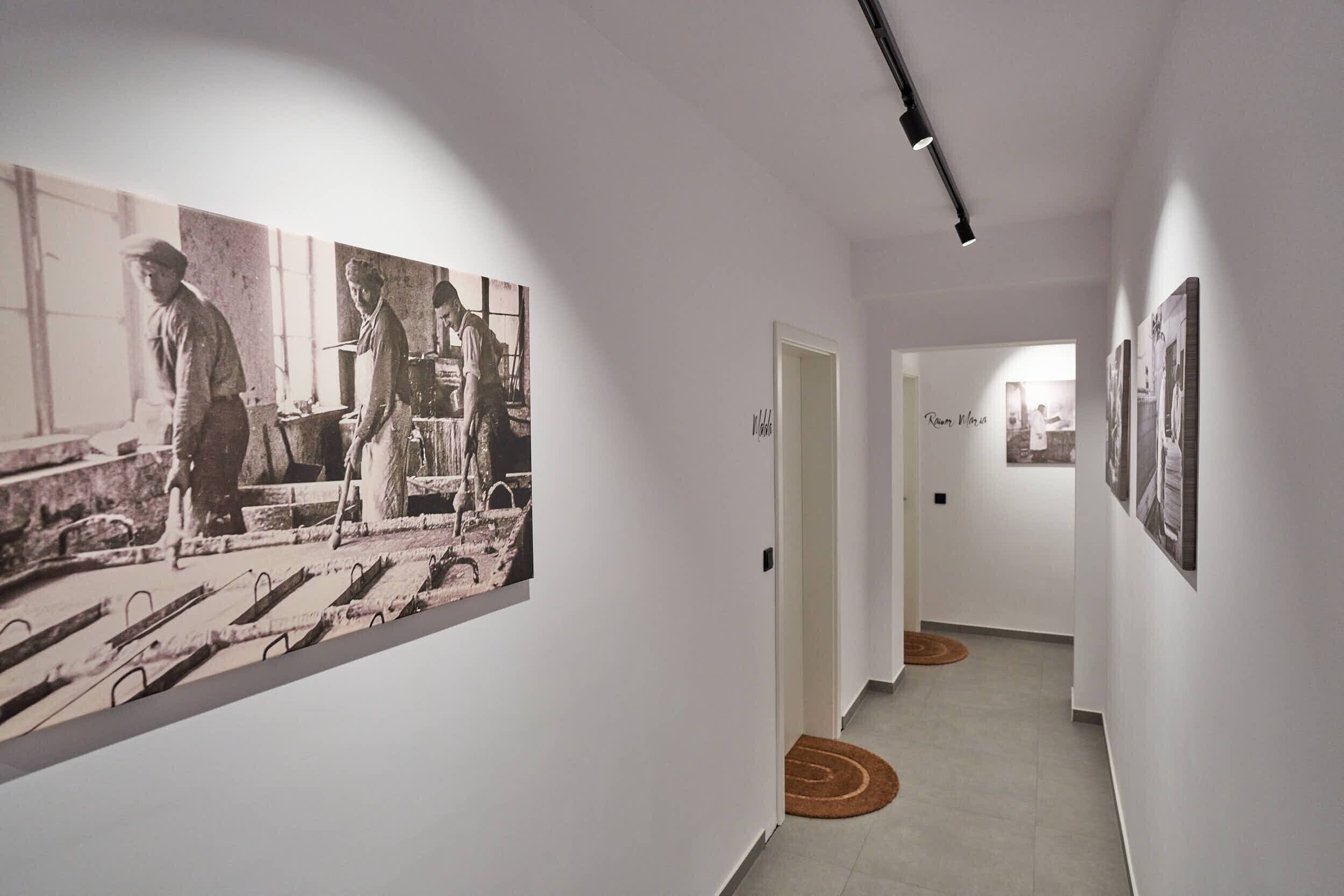 Un couloir aux murs blancs, orné de photographies en noir et blanc, et éclairé par un luminaire.