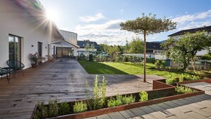 Eine moderne Terrassenduschel mit Holzboden, einem Rasen und einem Baum.