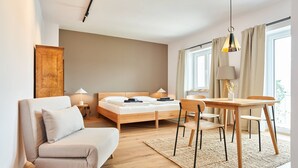 Un dormitorio moderno con cama, mesitas de noche, sofá, mesa de comedor y ventana con cortinas.