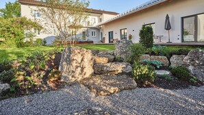Una casa moderna con un jardín cuidado, un patio con mobiliario exterior y un ventanal grande.