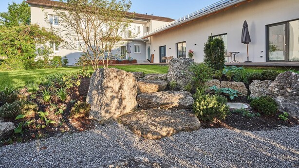 Una casa moderna con un jardín cuidado, un patio con mobiliario exterior y un ventanal grande.