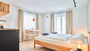 Een moderne hotelkamer met een houten bed, een bureau met een waterkoker, een stoel en een kleine tafel met een lamp.