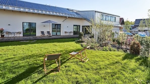 Een modern gebouw met een dak van zonnepanelen, een gazon met terrasmeubilair en een heldere lucht.