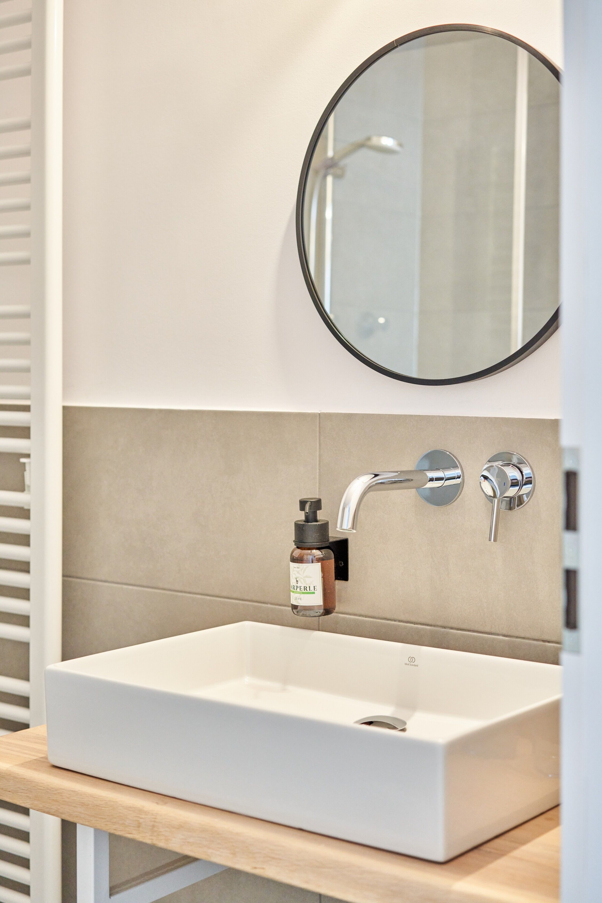 Un bagno con un lavandino bianco, uno specchio tondo e una saponetta.