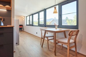 Una habitación con mesa y sillas, ventanas amplias, una lámpara colgante y vistas a un edificio y árboles.