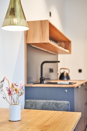 Una cocina moderna con una mesa de madera, un florero blanco con flores secas y una lámpara colgante.