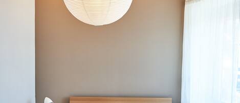 A bedroom with a double bed, two bedside tables, a nightstand, and a hanging light fixture.