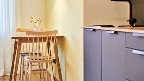 Un comedor con mesa y sillas de madera, una lámpara colgante, un mueble con cajones y un ventanal con cortinas.