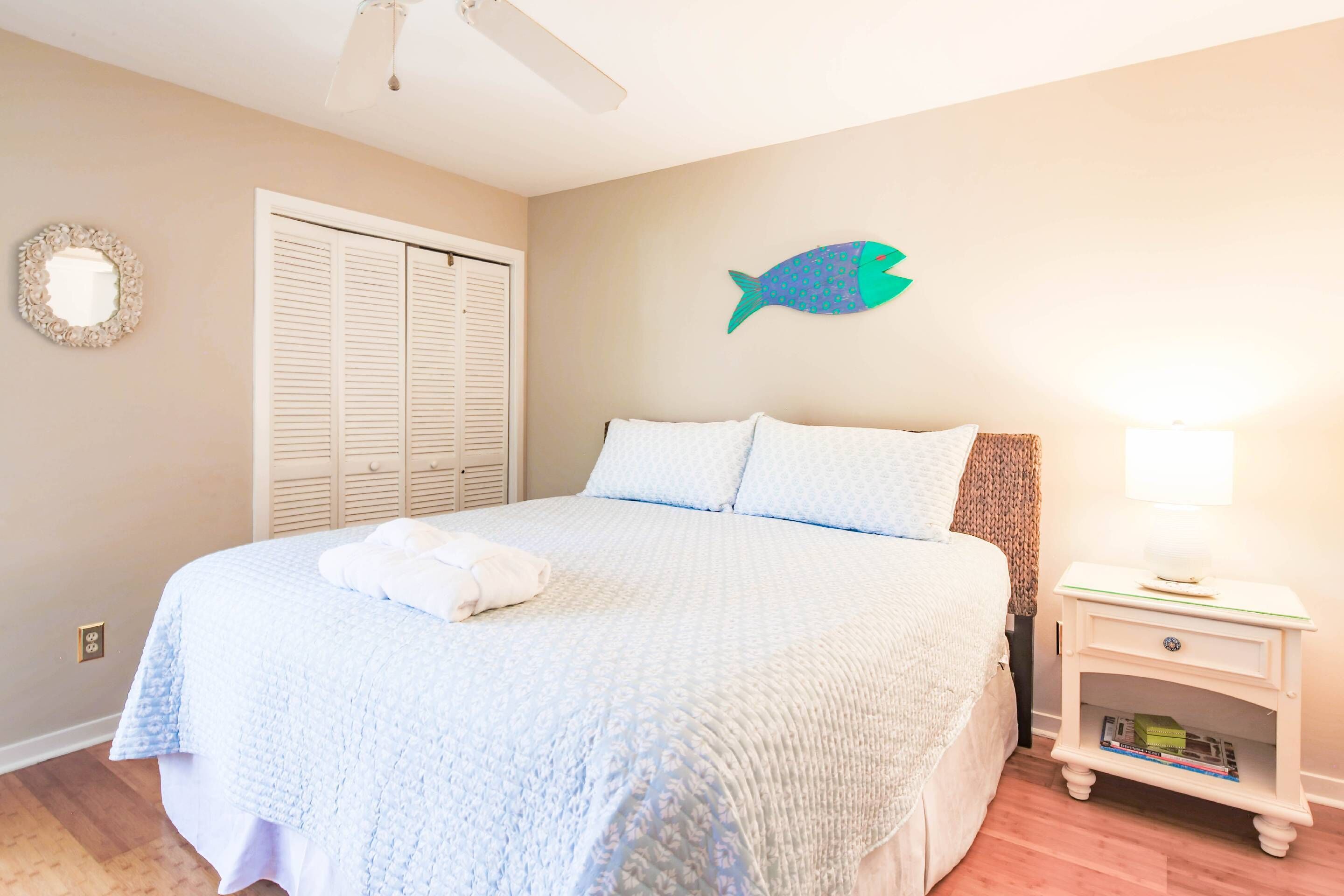 A bedroom with a bed, a nightstand, a wall-mounted fish decoration, a door, and a ceiling fan.