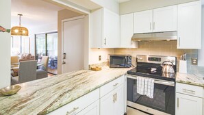 Une cuisine moderne avec des meubles blancs, un plan de travail en granit, un four à micro-ondes, une cuisinière et un coin repas visible à travers une porte ouverte.