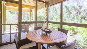 Un espace extérieur aménagé avec une zone salon couverte, comprenant une table ronde et des chaises en osier, donnant sur un jardin luxuriant.