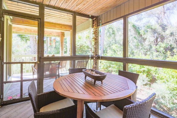 A covered outdoor seating area with a round table and wicker chairs, overlooking a lush garden.