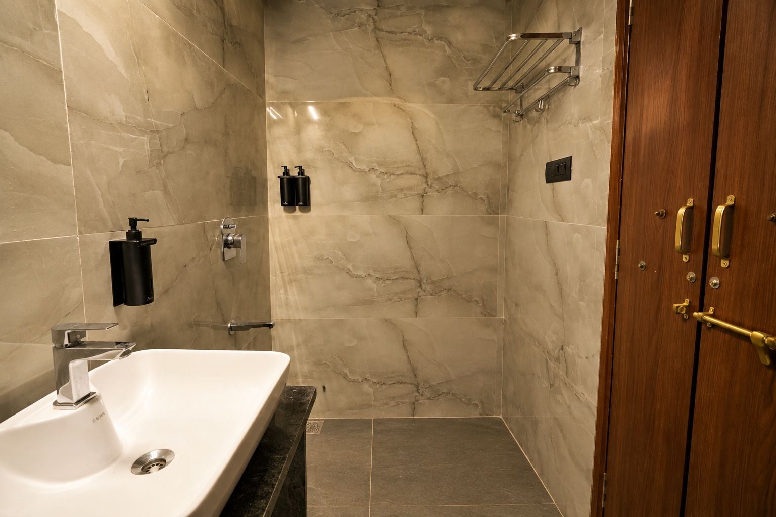 A bathroom with a marble wall, a sink, a shower, and a wooden door.