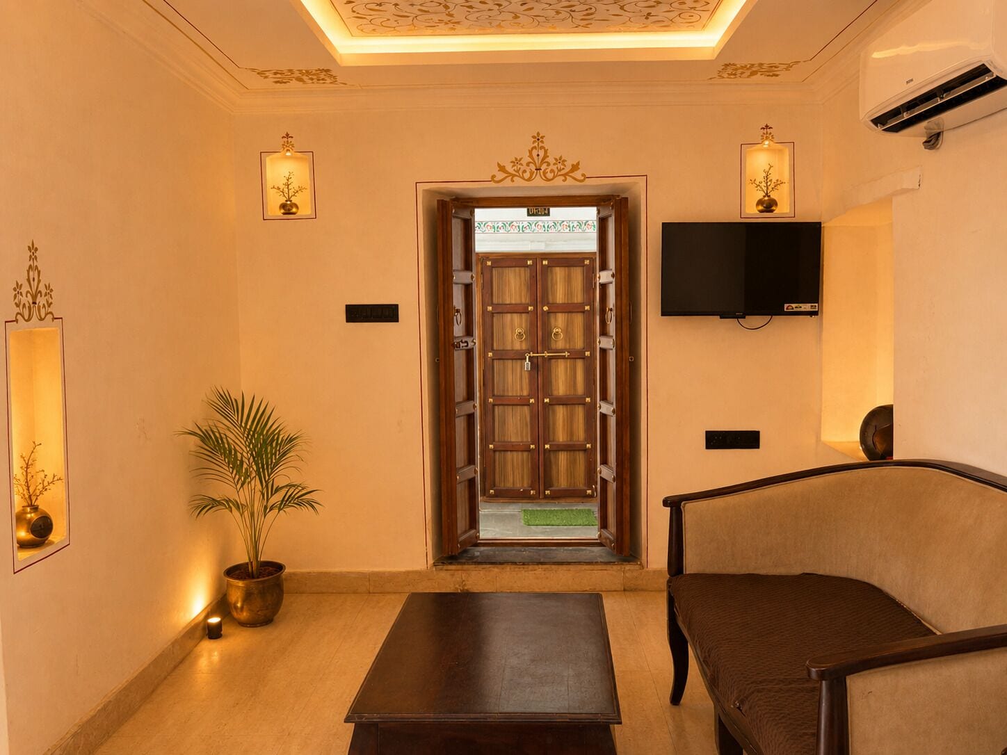 A lobby with a wooden door, a television mounted on the wall, a potted plant, and a sofa.