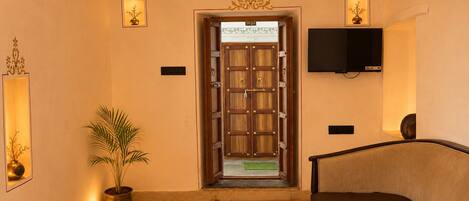 A lobby with a wooden door, a television mounted on the wall, a potted plant, and a sofa.